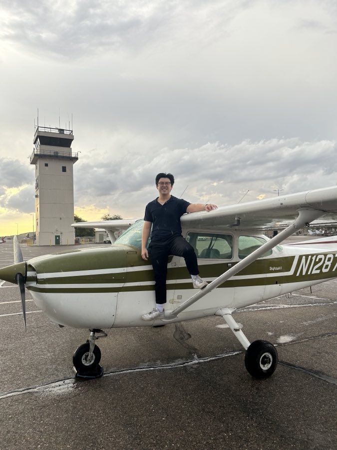 A student sitting on the cowling of N1287U at dusk, control tower behind